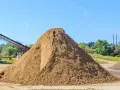 Ogromna hałda piasku na placu budowy, zastanawiasz się, ile kosztuje tona piasku? W tle taśmociąg i drzewa.