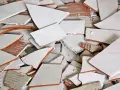 Stos białych, połamanych płytek ceramicznych z pomarańczowymi krawędziami. Wskazówka, jak zdjąć płytki ze ściany bez uszkodzenia.