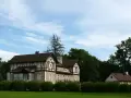 Elegancki dom z charakterystyczną konstrukcją szachulcową, otoczony zielenią, pod błękitnym niebem z chmurami.