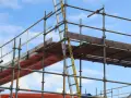 Rusztowanie aluminiowe z drabiną na tle błękitnego nieba.