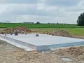 Płyta betonowa, czyli fundament, gotowa do budowy domu. Wokół piasek i zielone pola.