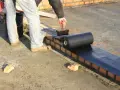Pracownik nakłada **abizol** na ceglaną ścianę, przygotowując izolację dachu.
