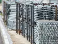 Stosy aluminiowych elementów rusztowania stojące na placu budowy.