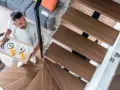 Mężczyzna niesie śniadanie po nowoczesnych schodach policzkowych z drewnianymi stopniami i szklaną balustradą.