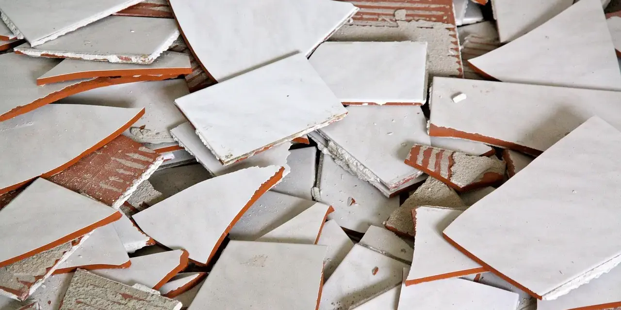 Stos białych, połamanych płytek ceramicznych z pomarańczowymi krawędziami. Wskazówka, jak zdjąć płytki ze ściany bez uszkodzenia.