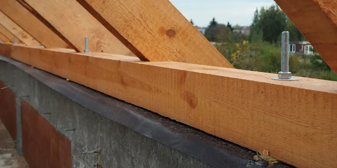 Drewniana murłata przymocowana do betonowej ściany za pomocą śrub.