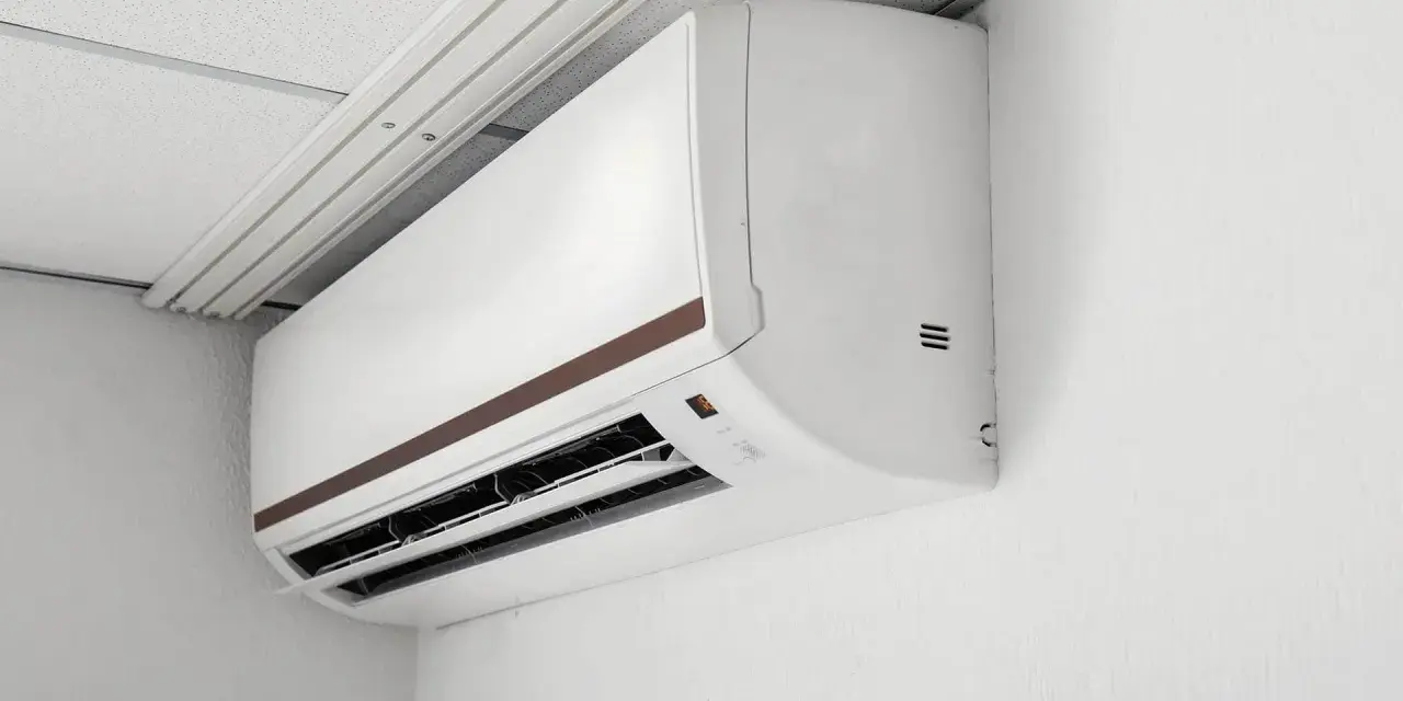 Biała jednostka klimatyzacyjna zamontowana na ścianie pod sufitem podwieszanym.
