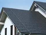 Ciemnoszara dachówka, czy to dachówka betonowa, czy ceramiczna, pokrywa dwa spadziste dachy domu pod błękitnym niebem.