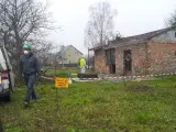 Pracownicy w kombinezonach usuwają eternit z dachu. Tablica ostrzega przed zagrożeniem azbestem.