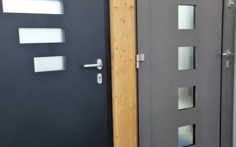 Dwie nowoczesne drzwi wejściowe, jedna ciemnoszara z prostokątnymi przeszkleniami, druga szara z kwadratowymi. Dowiedz się, jak uszczelnić drzwi wejściowe.