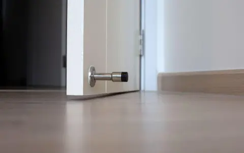 Metalowy odbojnik zamontowany na dole białych drzwi, zapobiegający ich trzaskaniu.