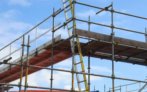 Rusztowanie aluminiowe z drabiną na tle błękitnego nieba.