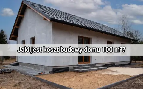 Szary dom w trakcie budowy, z widocznym dachem i oknami. Na froncie napis "Jaki jest koszt budowy domu 100 m²?".