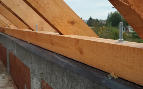 Drewniana murłata przymocowana do betonowej ściany za pomocą śrub.