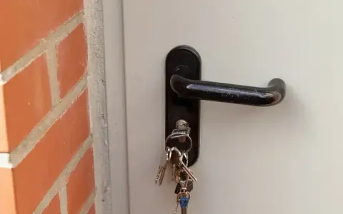 Klucze wiszą przy zamku w białych drzwiach. Zastanawiasz się, ile kosztuje wymiana zamka w drzwiach?