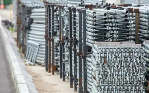 Stosy aluminiowych elementów rusztowania stojące na placu budowy.
