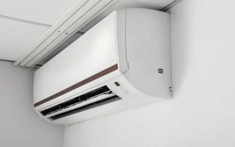 Biała jednostka klimatyzacyjna zamontowana na ścianie pod sufitem podwieszanym.