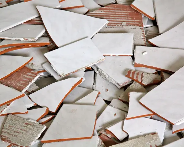 Stos białych, połamanych płytek ceramicznych z pomarańczowymi krawędziami. Wskazówka, jak zdjąć płytki ze ściany bez uszkodzenia.