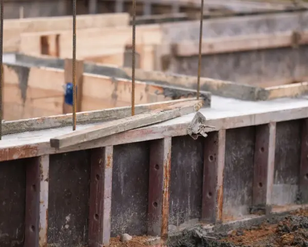 Drewniany szalunek czeka na beton. Widać zbrojenie i świeży beton.