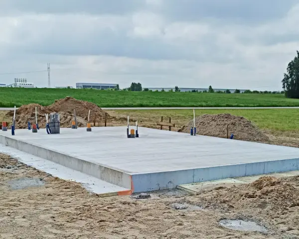 Płyta betonowa, czyli fundament, gotowa do budowy domu. Wokół piasek i zielone pola.