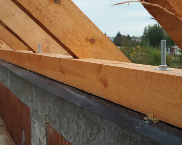 Drewniana murłata przymocowana do betonowej ściany za pomocą śrub.