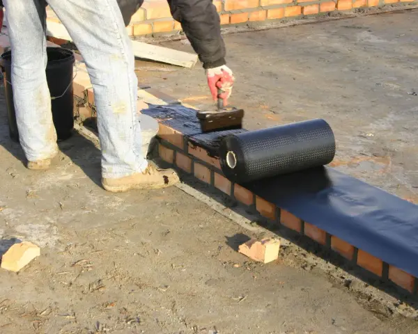 Pracownik nakłada **abizol** na ceglaną ścianę, przygotowując izolację dachu.