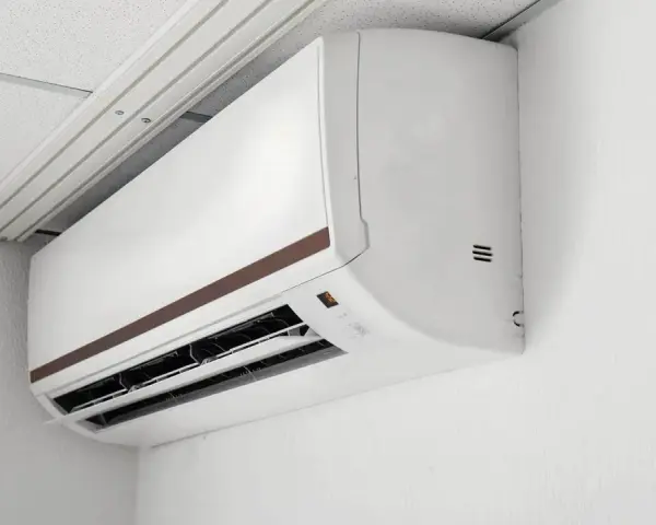 Biała jednostka klimatyzacyjna zamontowana na ścianie pod sufitem podwieszanym.