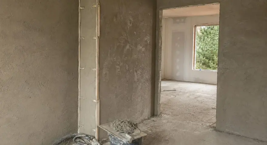 Ściany pokryte surowym tynkiem wapienno cementowym, gotowe do dalszych prac. Widać wiadro z zaprawą i narzędzia.