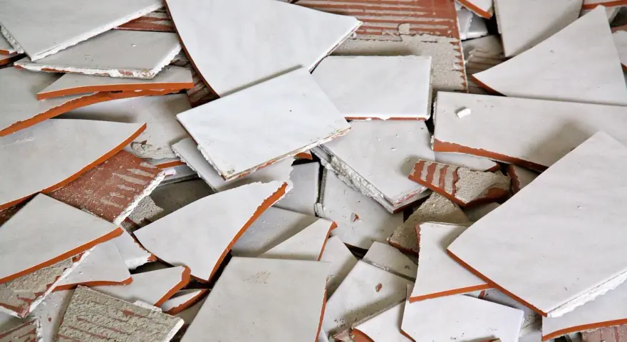 Stos białych, połamanych płytek ceramicznych z pomarańczowymi krawędziami. Wskazówka, jak zdjąć płytki ze ściany bez uszkodzenia.