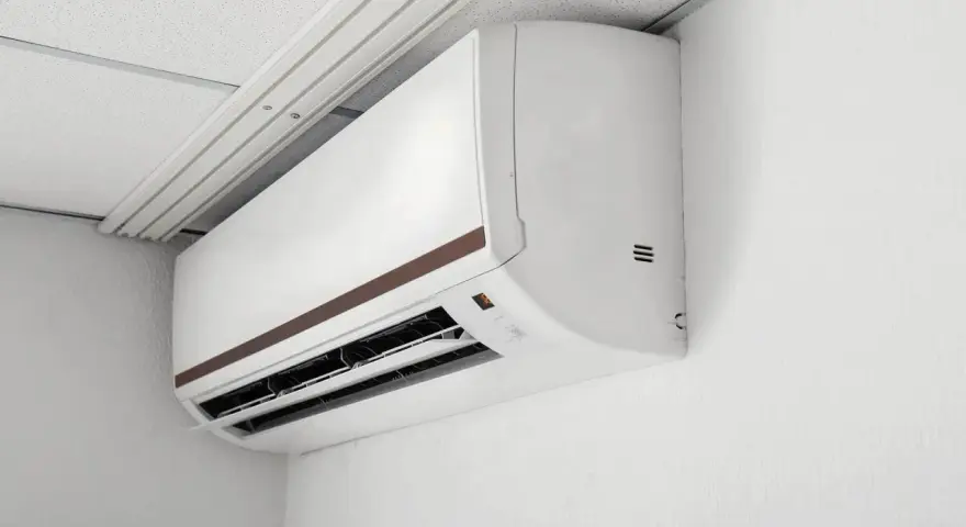 Biała jednostka klimatyzacyjna zamontowana na ścianie pod sufitem podwieszanym.